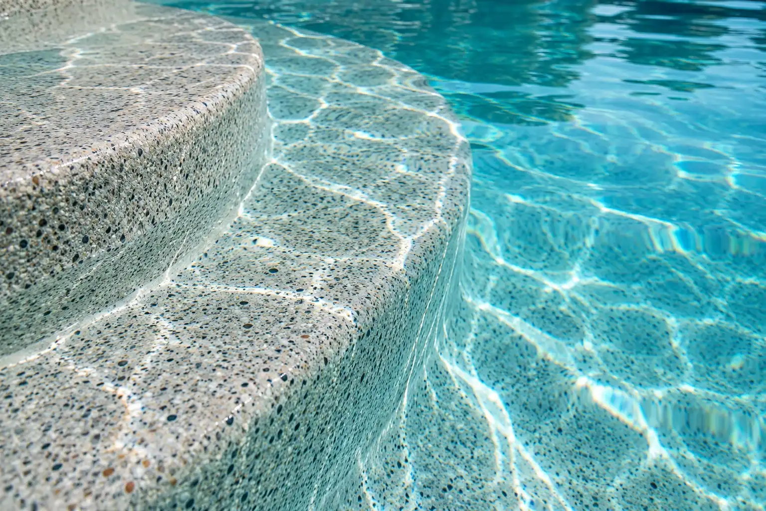 Close view of a fine pebble finish on curved pool steps under clear water